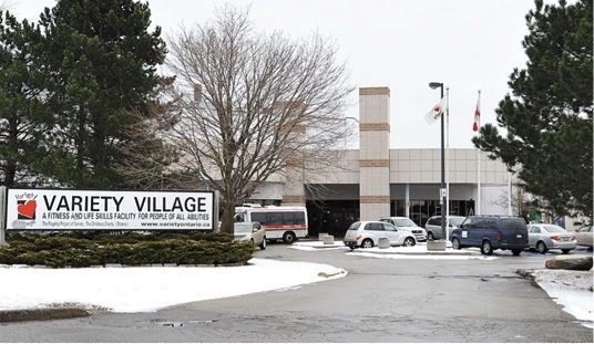 This image is of a photograph that shows the exterior of the Variety Village building during the winter. A sign on the left-hand side of the photo reads “Variety Village A Fitness And Life Skills Facility For People Of All Abilities”.