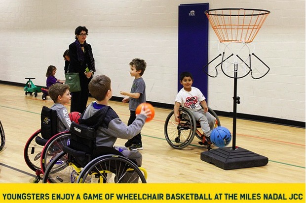 This image is of a photograph that shows several children playing basketball, using wheelchairs in a gymnasium setting.